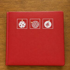 Red book with three Christmas ornaments on it, sitting on a wooden surface